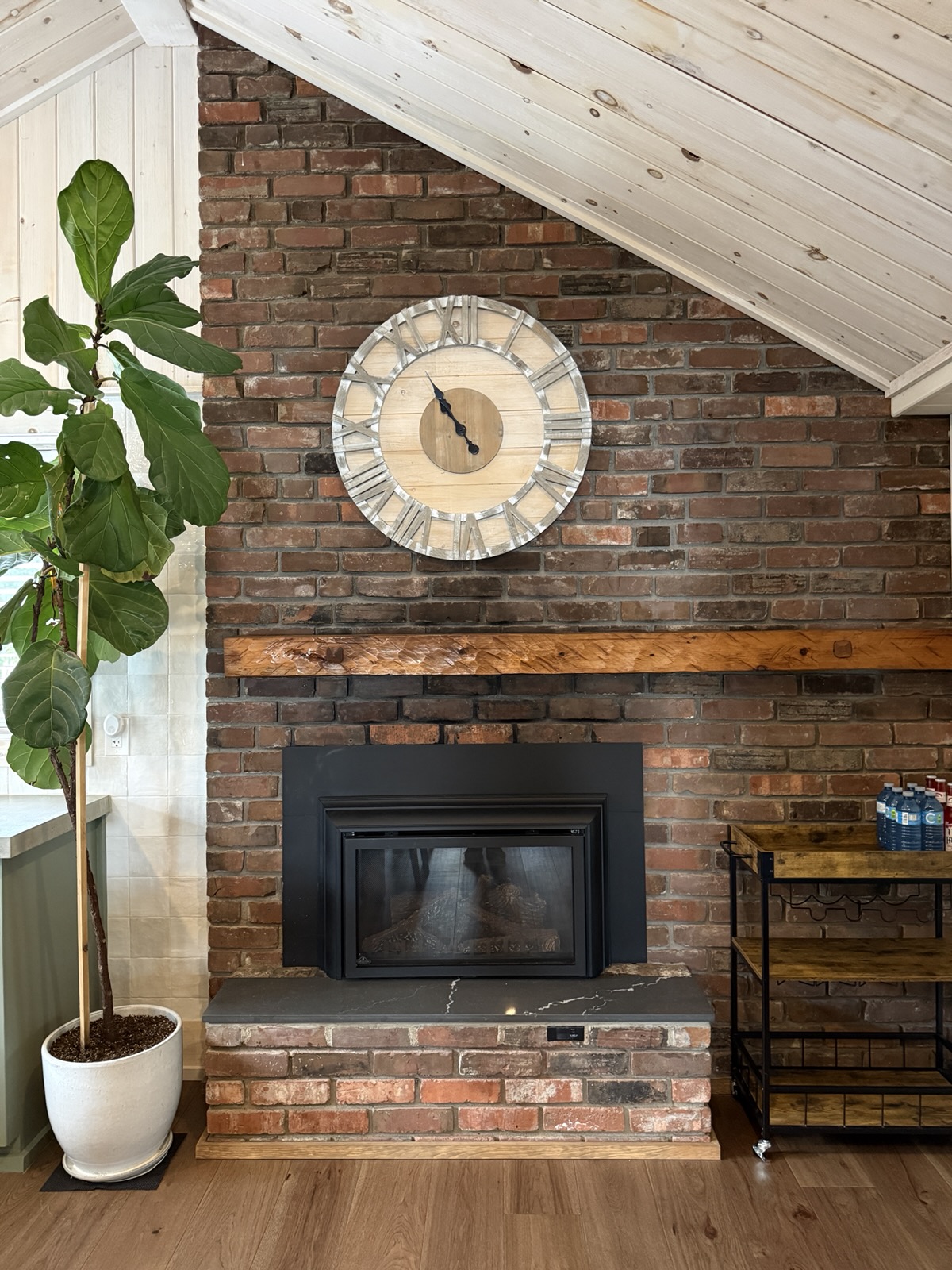 The brick fireplace with a large clock and a fiddle leaf fig